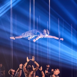 acrobat suspended in the air above a group of hands ready to catch